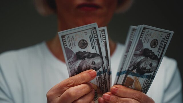 Old Caucasian woman counts the cash one hundred in hands, banknotes. Senior female holds paper money USD dollars in palms, with money deficit. Utility Bills Payment earnings. Elderly lady counting.