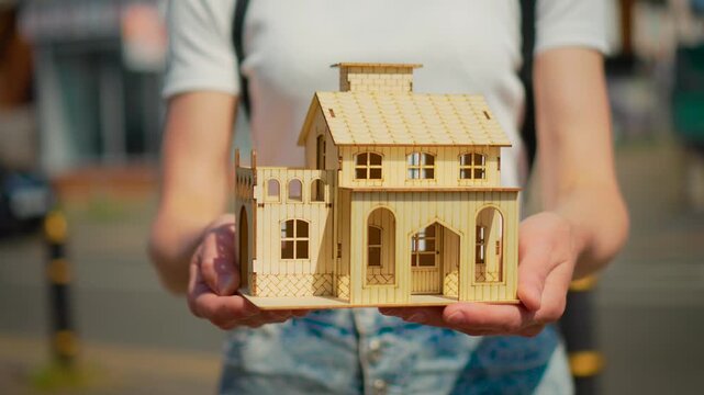 Housing offer concept with wooden house model in outstretched hands. Mortgage application and property purchase proposal with residential investment planning theme. New home opportunity and real