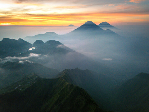 Aerial view of volcanic mountain peaks rising above a thick layer of mist and clouds during a vibrant sunrise in Indonesia.