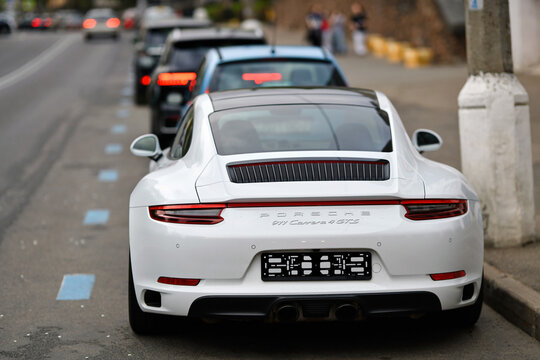 Minsk, Belarus. May 5, 2026. Rear view of white Porsche 911 Carrera 4 GTS sports car parked on street, red taillights black spoiler and dual exhaust pipes on city road with blurred background cars