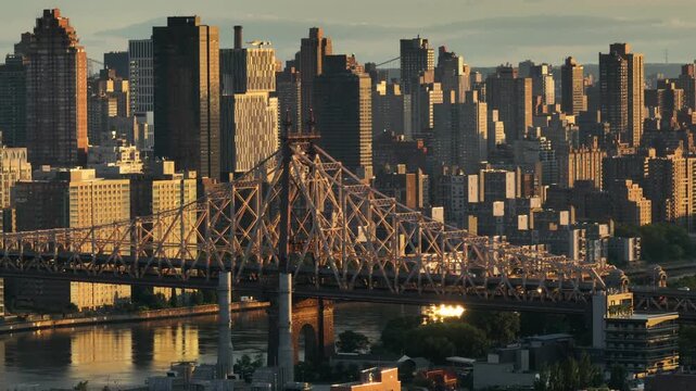 A cinematic aerial view of ed koch queensboro bridge at sunset, new york city skyline background, golden hour traffic movement.