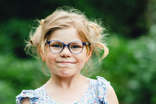 Portrait of funny little girl with glasses making playful face outdoors with messy hairstyle and cheerful expression