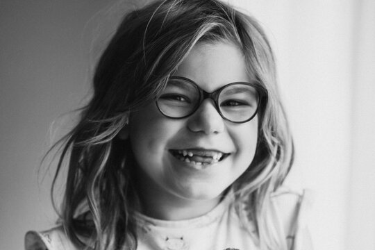 Laughing young girl with glasses smiling in black and white portrait showing natural teeth gap and joyful childhood expression