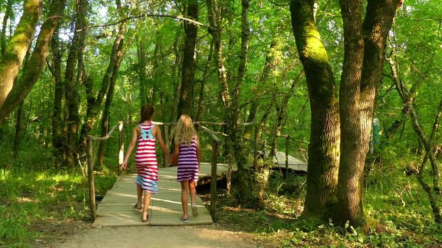 Little girls walk on wooden walkways in a beautiful green park.
