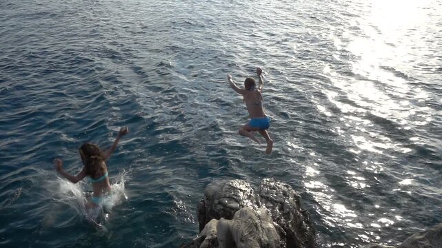 Little beautiful girl jumping from stone to sea