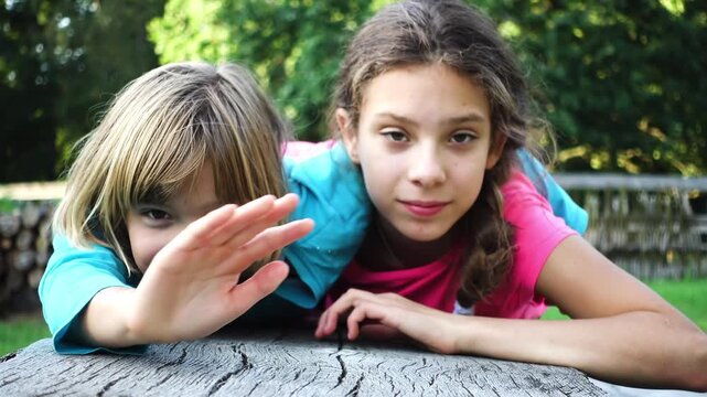 Two little sisters lie on a wooden bench in a summer city park.