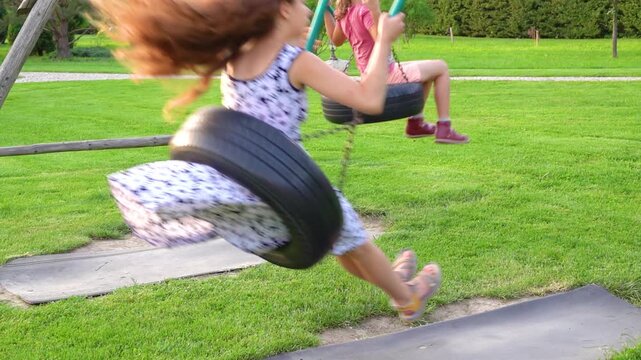 Two sisters swinging on a swing from a car tire.