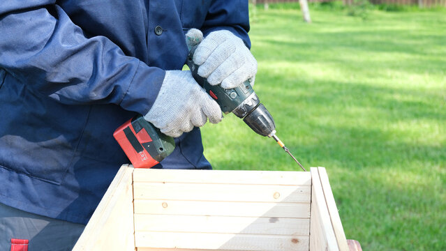 Worker man working with Screwdriver. Person using a red cordless drill with a metal spiral drill bit in a workshop, construction, diy project task. Accu battery hand drill. Screwing a screw assembling