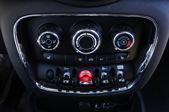 Close up car climate control panel. Premium dashboard climate panel with chrome rings rotary dials for fan temperature and air flow plus illuminated red start engine stop button. It highlights advance