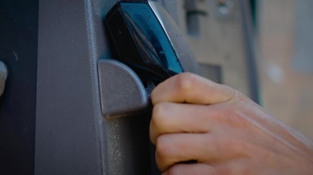Hanging up receiver on weathered public telephone booth after completed conversation. Closeup hand placing payphone handset back on vintage street communication device. Obsolete telecommunications