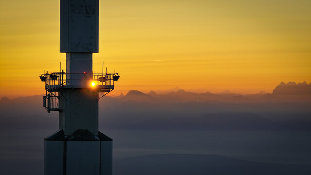 Aerial view of the Aiguille du Midi tower silhouette with a sun flare on the platform and the Mont Blanc massif peaks in the background Chamonix, Auvergne-Rhone-Alpes, France.