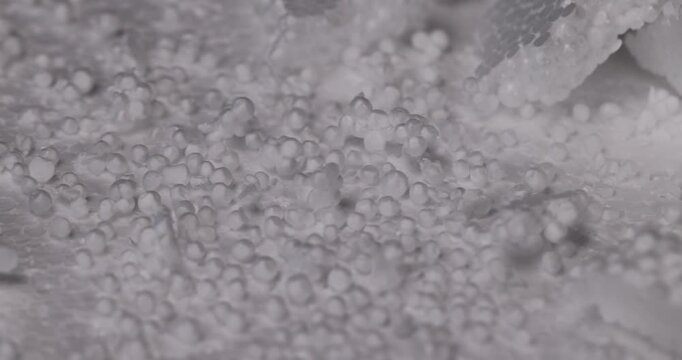 Small white foam balls and round foam granules are scattered over the light surface of the insulation board in a chaotic manner.