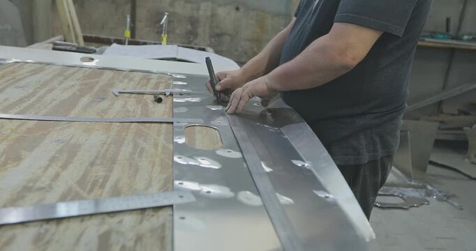 A boat designer marks out an aluminum sheet or plate on a workbench or table. Fabricating an aluminum hull for a modern aluminum boat. Shipyard, processing of an aluminum part. 
