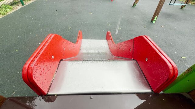 raindrops fall onto the metallic slide, creating a soft tapping sound. The empty and wet playground evokes a quiet, nostalgic, and lonely feeling.