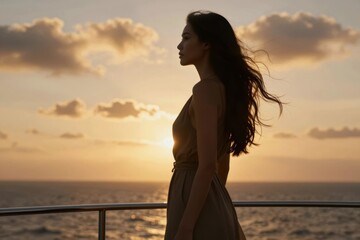 Fototapeta premium Woman stands on a boat deck as the sun sets over the ocean horizon in a warm glow