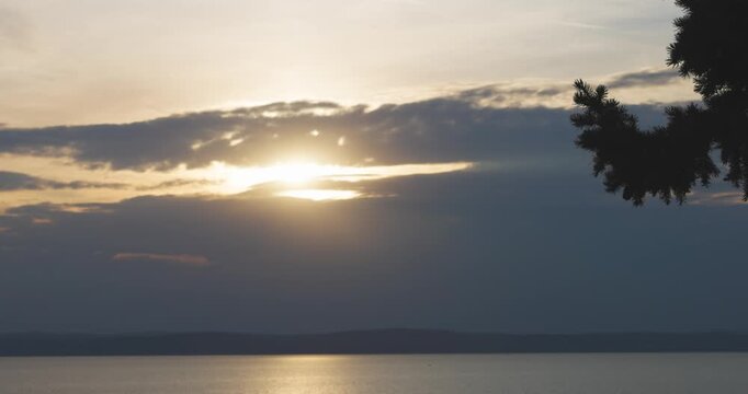 Sun reflecting on a calm lake surface with distant hills under a cloudy sky