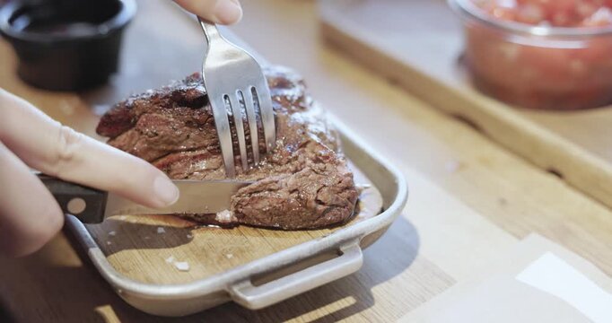 Person is cutting a delicious grilled beef steak with a knife and fork