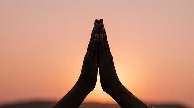 Silhouette of hands in prayer formation against a soft, gradient sunset sky