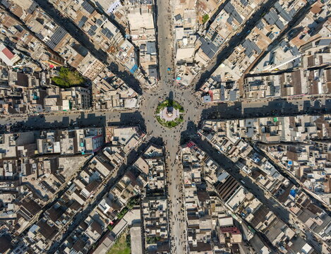 Aerial view of Clock Tower Faisalabad at the center of a radiating street pattern with dense urban buildings and solar panels on rooftops Faisalabad, Punjab, Pakistan.