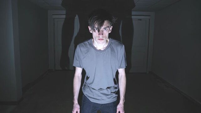 Man in dark hallway showing creepy poses for horror video. Scary guy acting weird with dramatic lighting in shadows. Cinematic footage with mysterious vibe for Halloween thrill or suspenseful scene