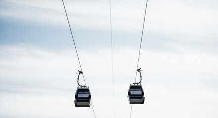 Obraz premium Two modern cable cars suspended on wires against a bright, overcast sky, offering scenic transport views