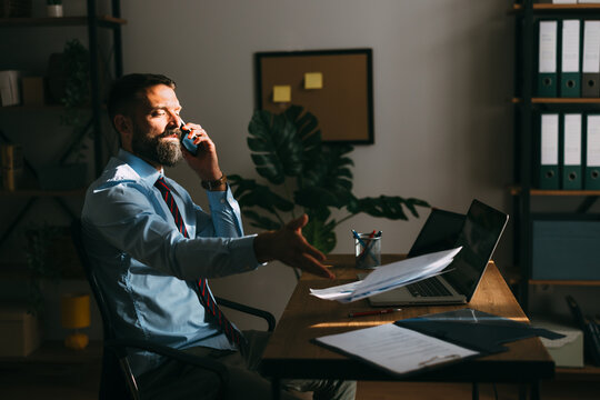 Stressed businessman talking on phone throwing paperwork in office