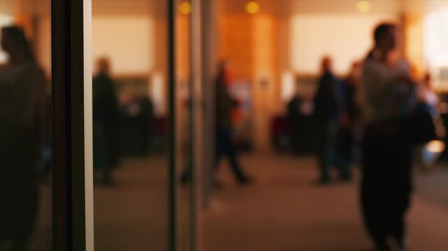 Blurred crowd of people walking through modern lobby entrance with warm light and reflections, 4K