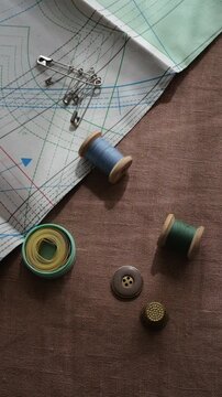 A spool of thread rolls across a brown linen fabric. Sewing accessories vertical video footage. 