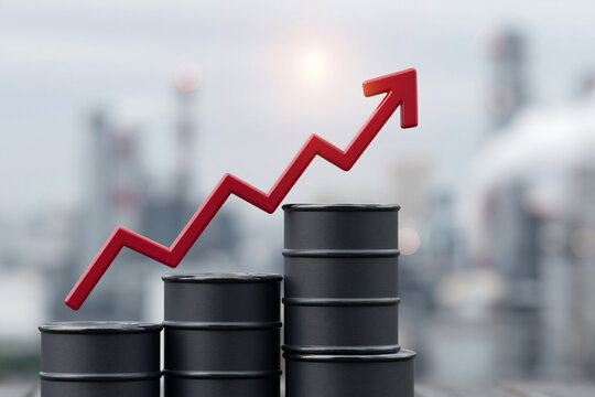 Red arrow rises above stacked oil barrels. Industrial backdrop hints at energy markets. Bright sun suggests growth and opportunity. Symbolic visuals convey rising demand
