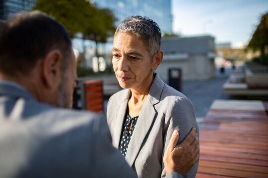 Mature businesswoman consoled by colleague in urban office plaza
