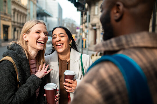 Three friends laughing over coffee on a city street