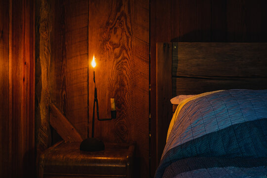 A pioneer-era reed lamp made with longleaf pine wood alongside a bed in a wood cabin in North Carolina