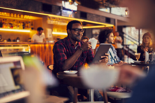 Man using tablet while drinking coffee in cozy cafe