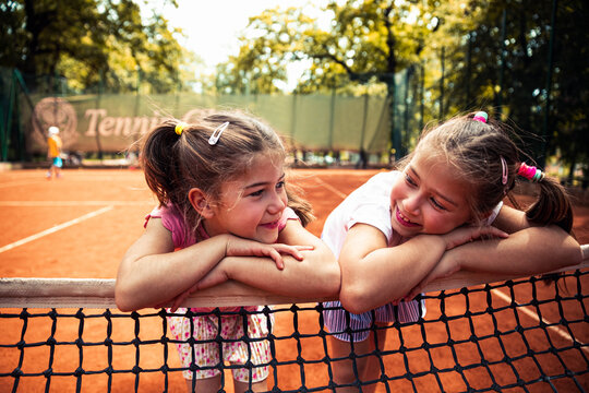 Two girls smiling over tennis net on outdoor clay court