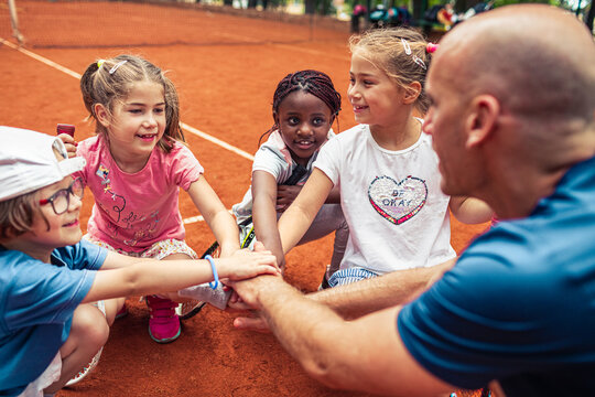 Kids with tennis coach huddle on clay court