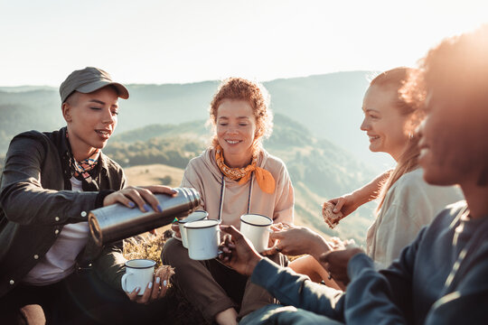 Friends sharing hot drinks on mountain hike at sunset