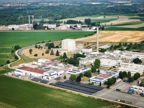 Aerial view of the Ex-Avogadro nuclear reactor facility with its containment dome and industrial structures surrounded by green fields in Saluggia, Piedmont, Italy.