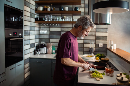 Middle-aged man chopping vegetables in modern home kitchen