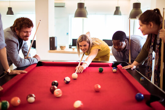 Coworkers playing pool in modern office break room