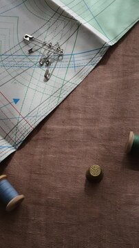 A seamstress's workplace. A spool of thread rolls. Pins, a thimble, patterns, linen fabric texture. 