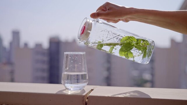 A person prepares mint water by pouring mint leaves into a jar. The jar is filled with water. The sun shines on the scene as this takes place in Benidorm