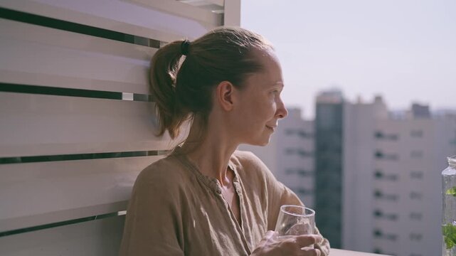 A person stands on a balcony in Benidorm, holding a glass. They look out at the city skyline as the sun sets. Thoughts fill their mind while enjoying the view