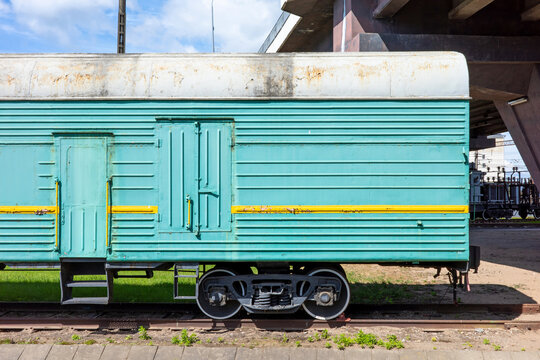 A weathered teal railway carriage sits stationary on train tracks beneath a concrete overpass, showcasing industrial character and aged textures.