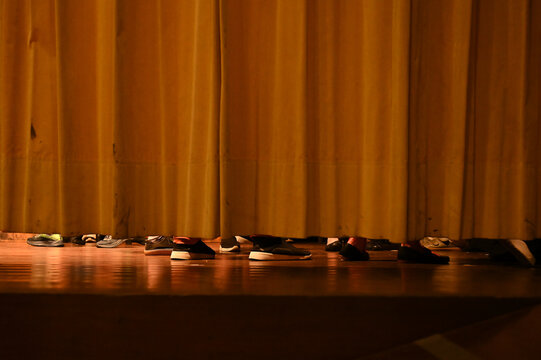 feet and shoes of performers visible under closed stage curtain, low angle snapshot of backstage preparation before theater play or graduation event, creative documentary style shot of theater stage 