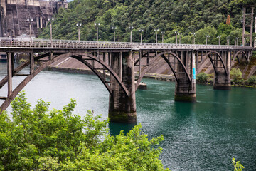 Fototapeta premium Arch Bridge at Hydropower Dam Over Green Reservoir
