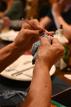 close up of artisan hands crocheting with grey yarn and hook, senior woman hands handcrafting textile item with needle, detailed macro view of traditional handmade crochet process indoors