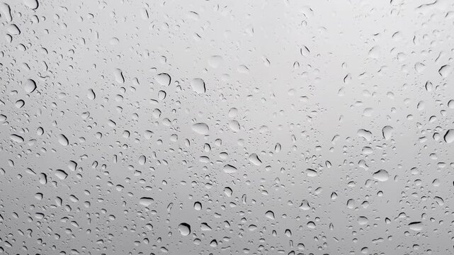 Raindrops on glass surface with light grey background texture, macro water drops on window