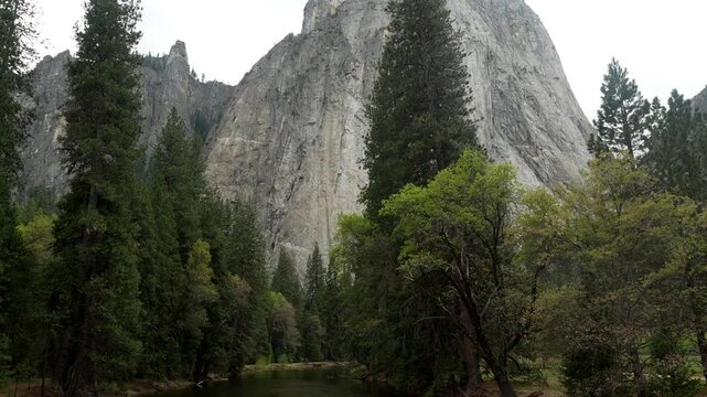 Majestic granite monolith of el capitan towering above the lush green forest and reflecting in the calm waters of the merced river on a cloudy day in yosemite valley, california