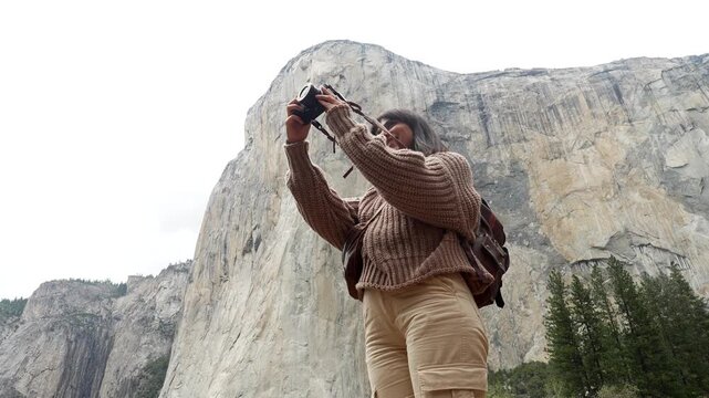 Young female traveler with a backpack smiling and using a professional camera to take pictures of the majestic el capitan granite monolith in yosemite national park, california