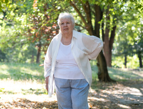 Senior woman feels pain while walking in park on summer day